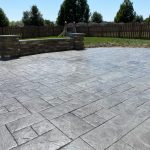 Our Work: Transforming a backyard with a stunning concrete patio enhanced by a captivating stone wall.