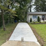 Our Work: A beautifully landscaped sidewalk leading up to a house surrounded by lush green grass and trees.