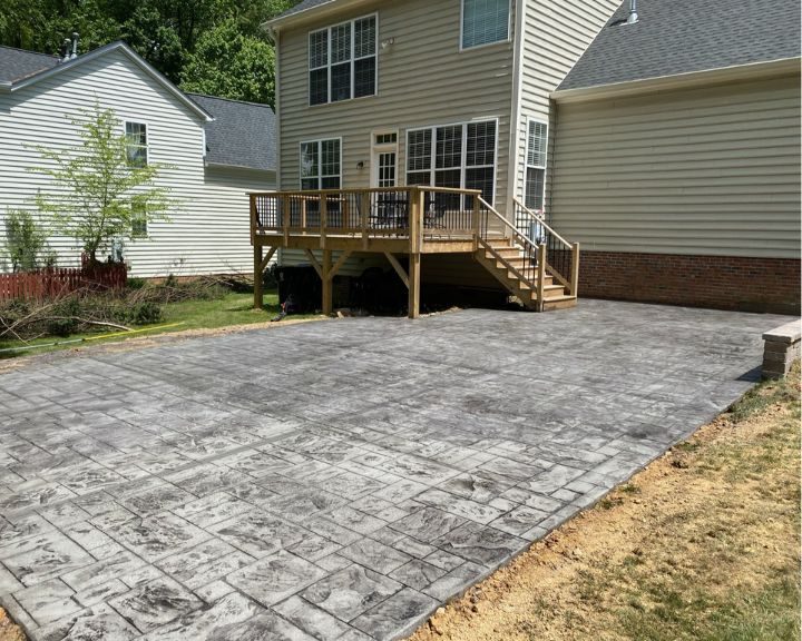 A concrete patio in a backyard with a deck. Looking for Concrete Contractors in Cary, NC? Look no further! We specialize in creating beautiful and durable concrete patios in your backyard, perfectly