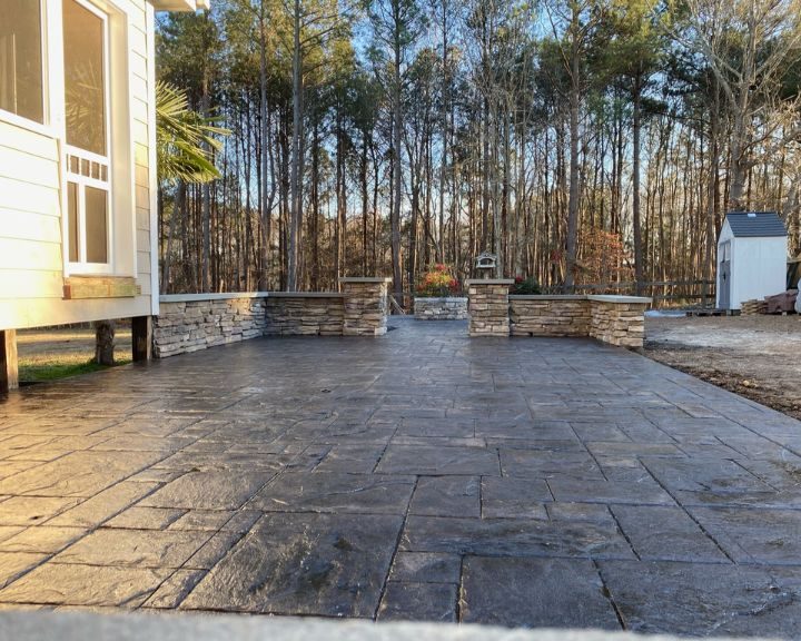 A patio with a concrete walkway and a stone fireplace.