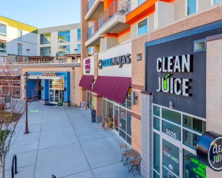 A view of a sidewalk with stores and a clean juice sign in one of the service areas.